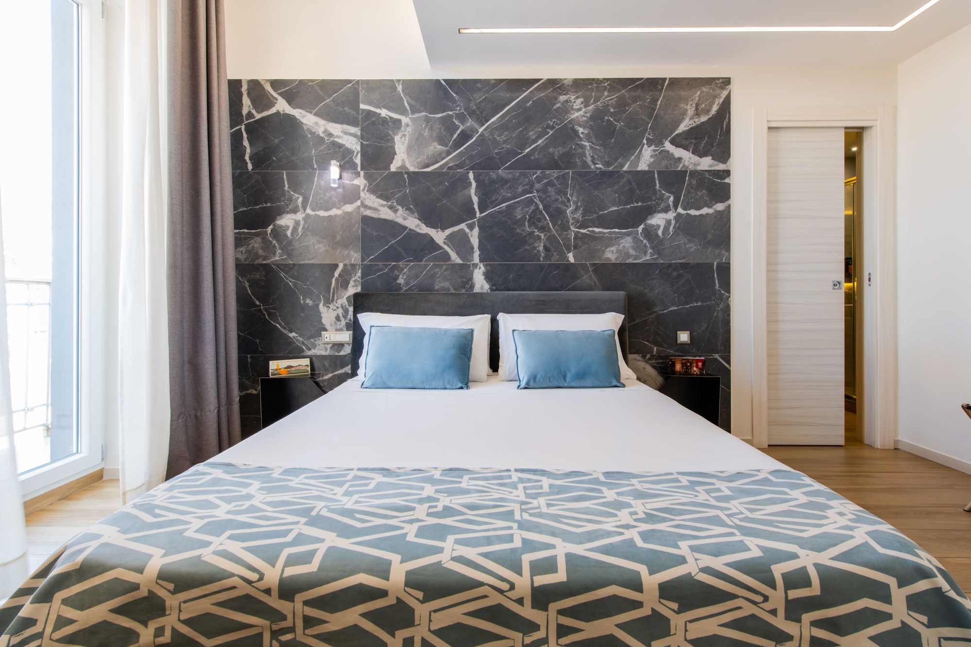 Camera Queen Deluxe con testiera in marmo grigio scuro e cuscini azzurri - Municipio Luxury Suite Napoli