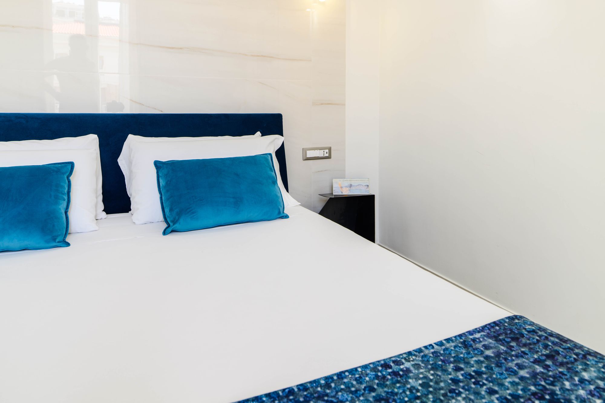 Dettaglio del letto con testiera blu velluto e comodino con set di benvenuto - Municipio Luxury Suite Napoli, foto 7