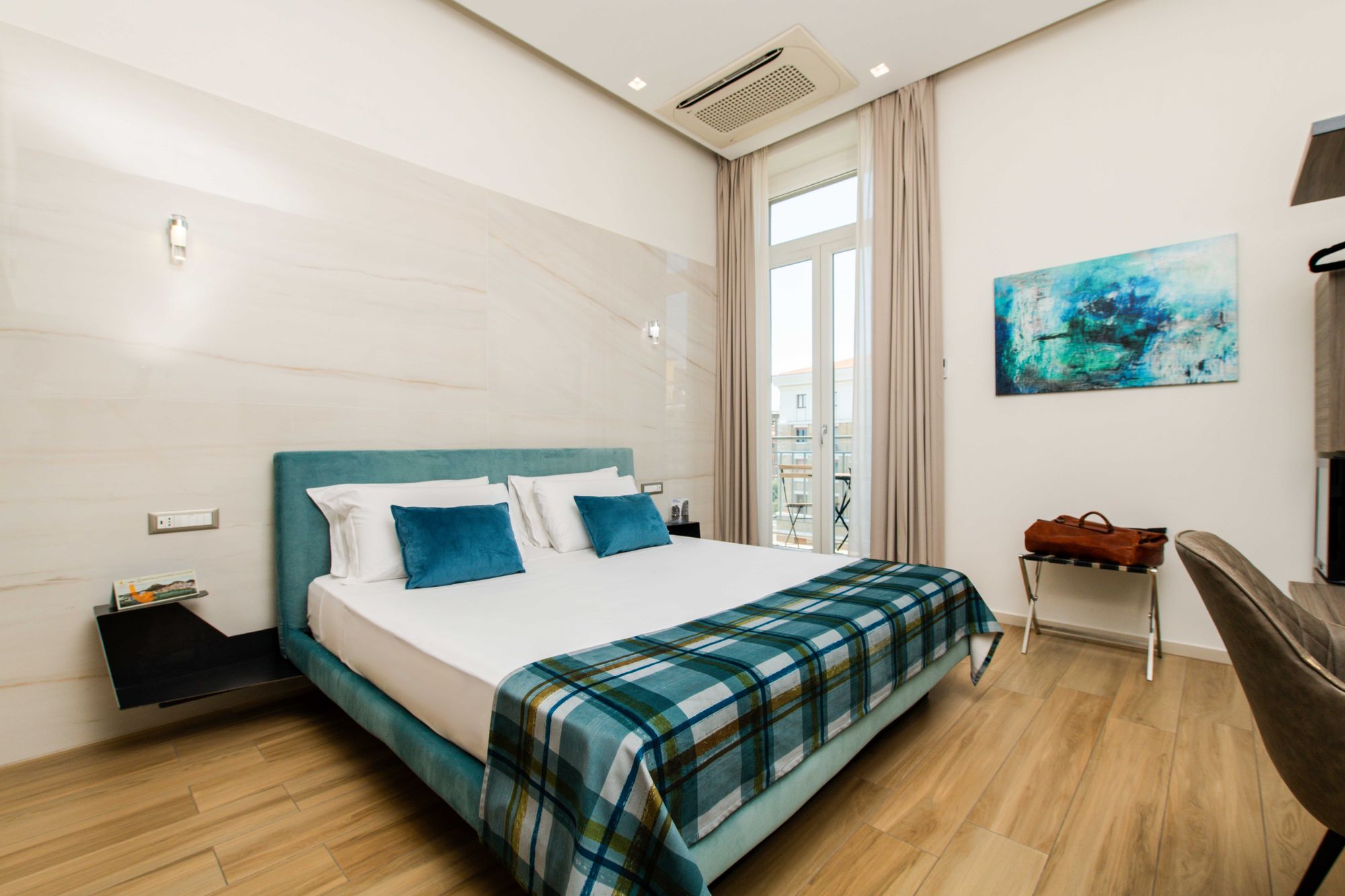 Letto con testiera verde acqua, cuscini blu e plaid a quadri, finestra con tenda, camera Napoli centro