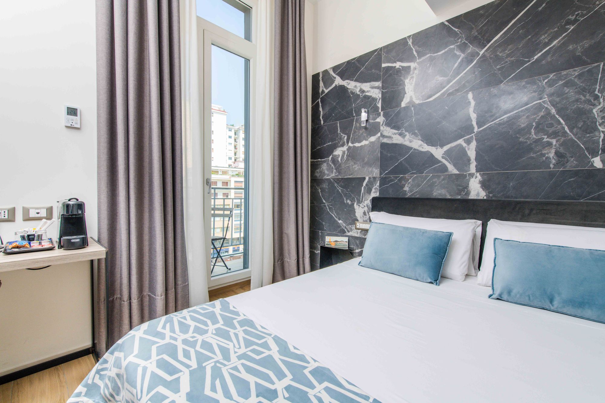 Dettaglio del letto con parete in marmo e cuscini in velluto azzuro, scrivania con macchina del caffè e finestra con vista - Municipio Luxury Suite Napoli, foto 8