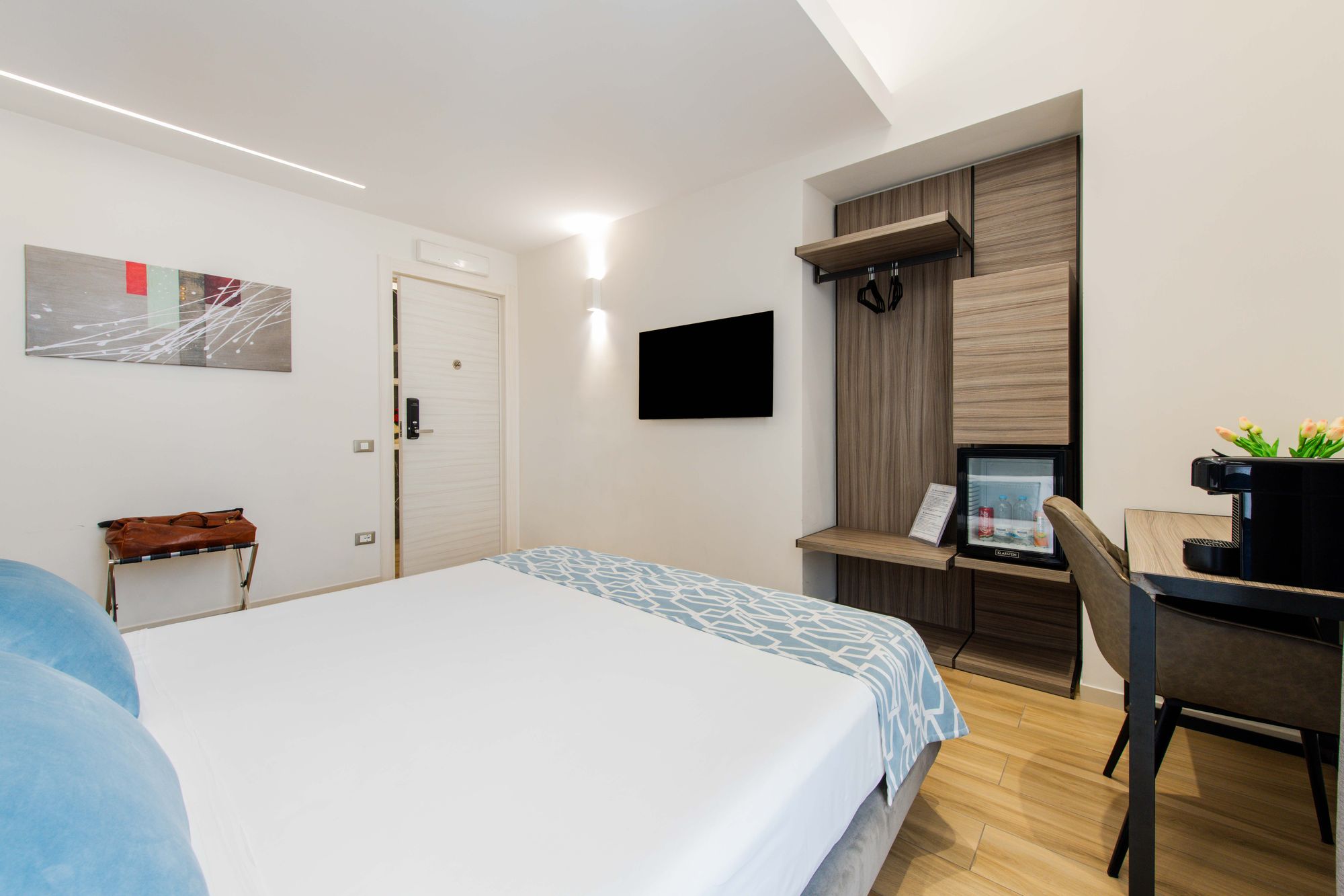 Letto matrimoniale con biancheria bianca e cuscino azzurro, scrivania con TV a parete - Municipio Luxury Suite Napoli, foto 3