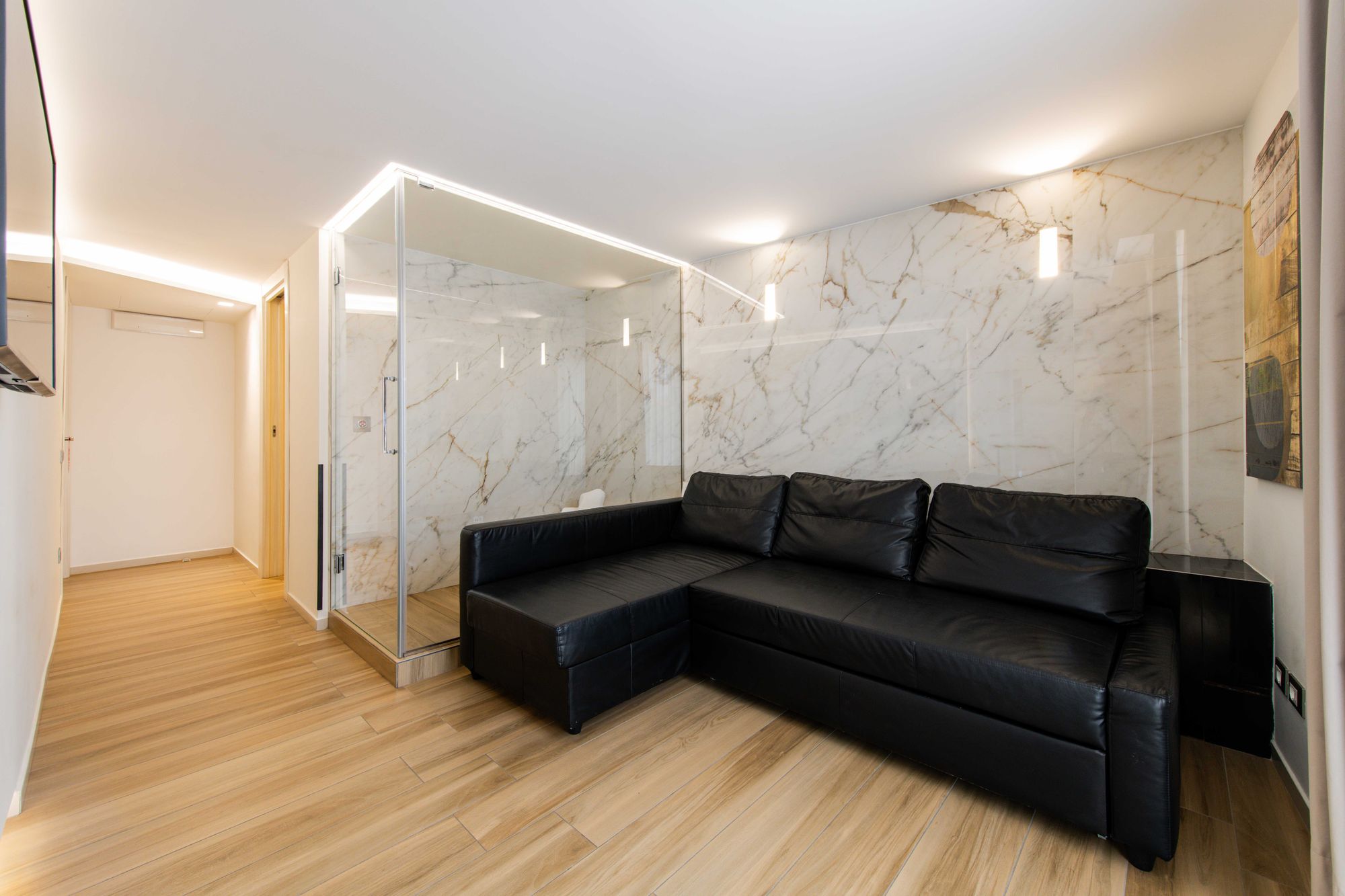 Zona living con sauna in vetro, pareti in marmo e divano ad angolo in pelle nera, suite Piazza Municipio Napoli