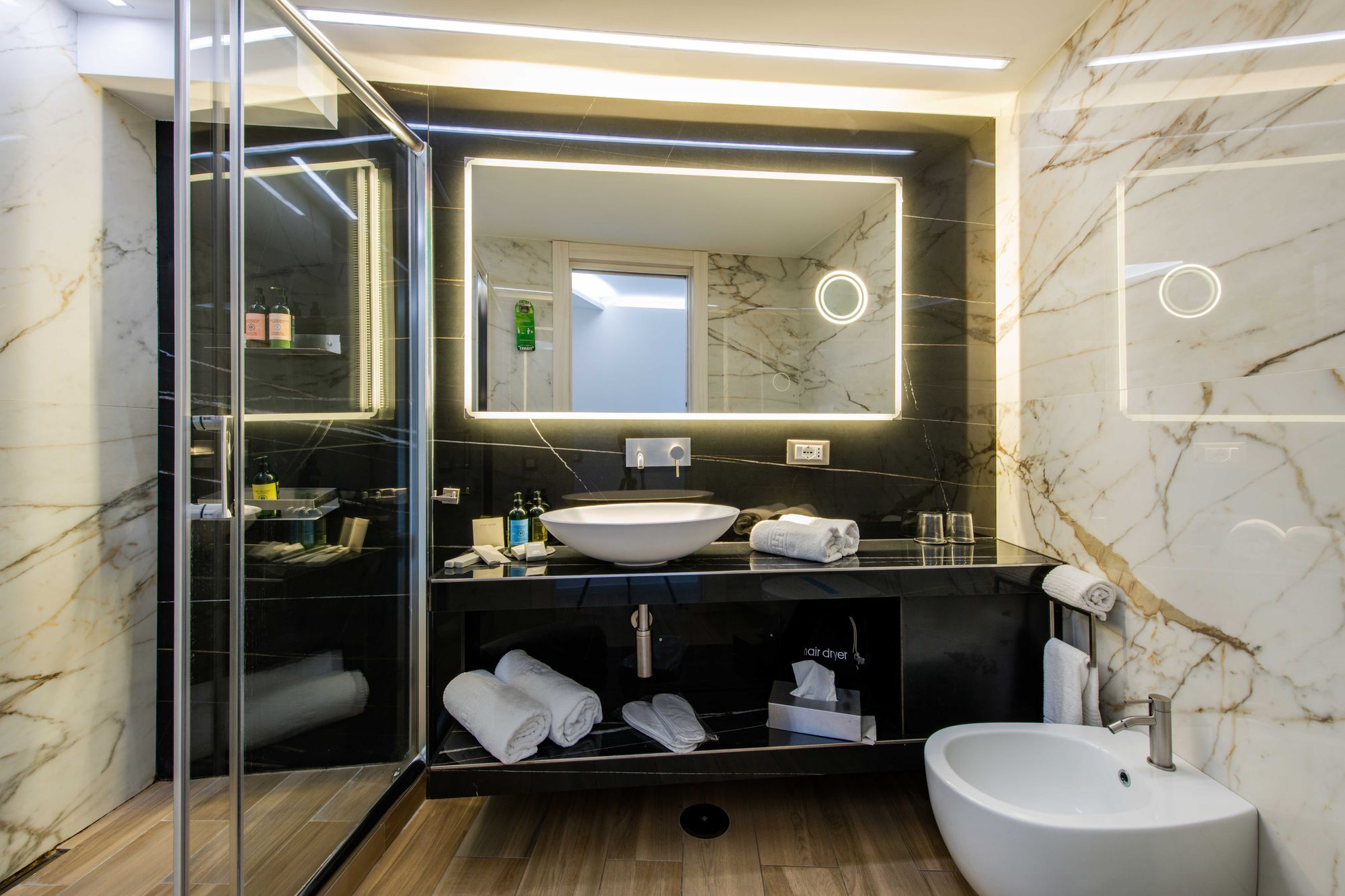 Bagno con lavabo, specchio e pareti in marmo beige, box doccia in vetro, suite con sauna Napoli