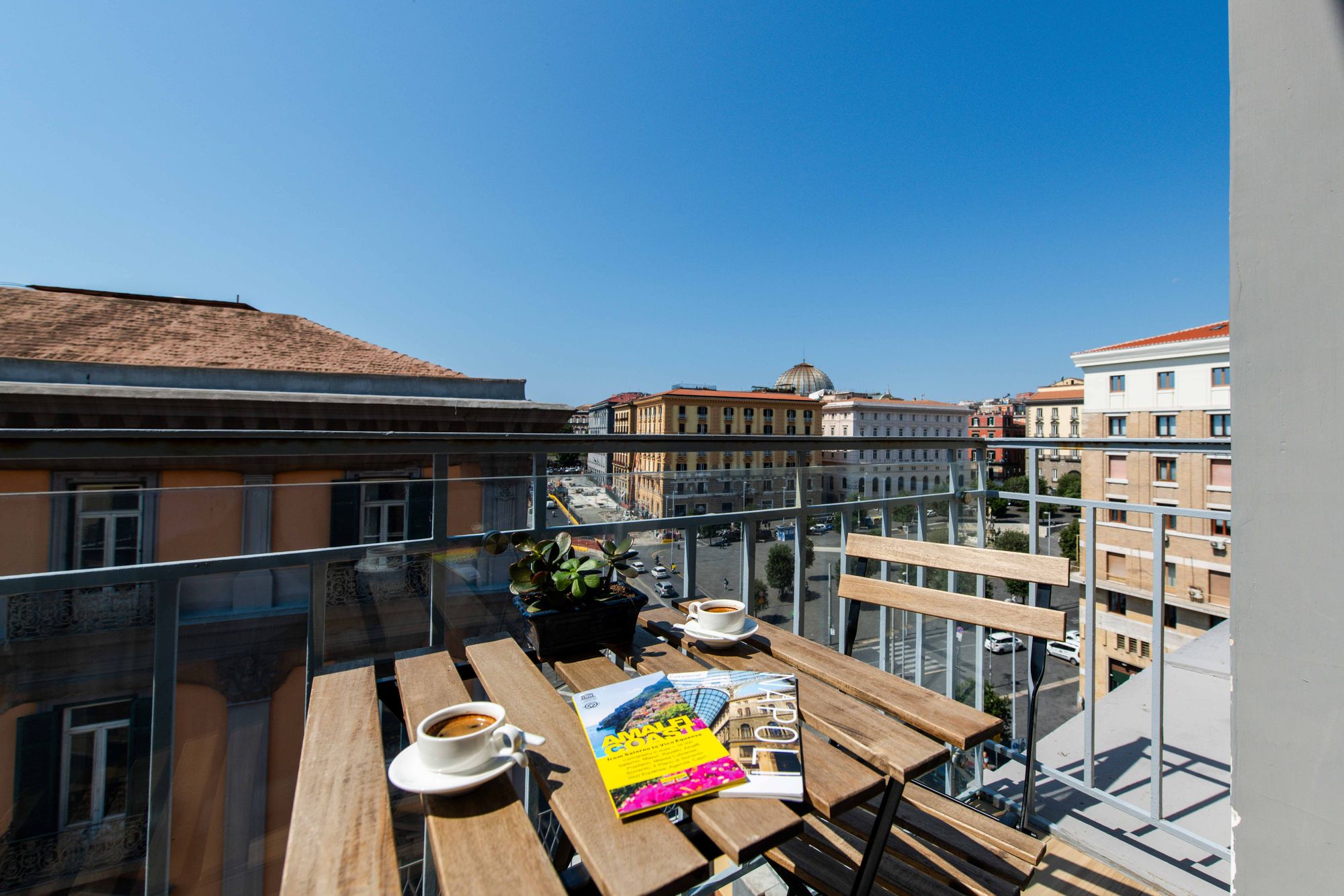 Balcone con tavolino, caffé e riviste, vista sugli edifici di Piazza Municipio Napoli