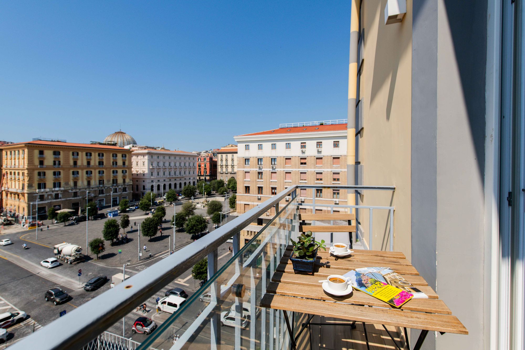 Vista dal balcone su Piazza Municipio con tavolino, caffè e riviste
